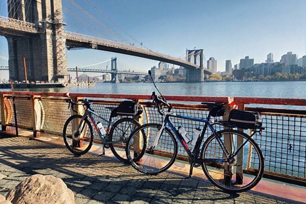 Bikes parked by the East River with Brooklyn Bridge and Manhattan skyline view — Hudson River Greenway bike route, Astra Bike Rentals NYC